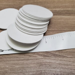 Pode incluir: Uma pilha de c&iacute;rculos de papel brancos redondos, com aproximadamente 7,6 cm de di&acirc;metro, ao lado de uma r&eacute;gua branca com marcas pretas.