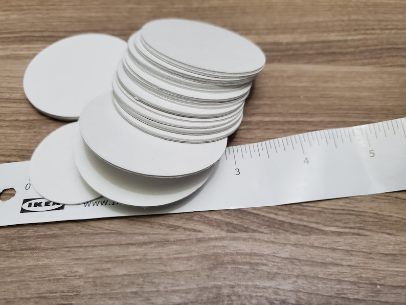 Pode incluir: Uma pilha de c&iacute;rculos de papel brancos redondos, com aproximadamente 7,6 cm de di&acirc;metro, ao lado de uma r&eacute;gua branca com marcas pretas.