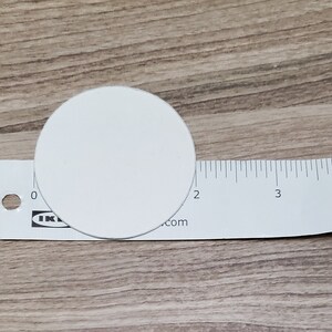 Pode incluir: Um c&iacute;rculo branco com 5 cm de di&acirc;metro, colocado em cima de uma r&eacute;gua branca com marcas pretas.