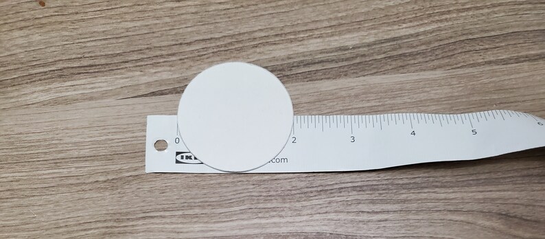 Pode incluir: Um c&iacute;rculo branco com 5 cm de di&acirc;metro, colocado em cima de uma r&eacute;gua branca com marcas pretas.