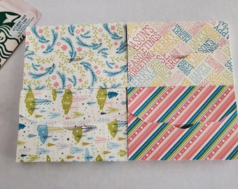 May include: Four different patterned gift card envelopes. The top two envelopes feature a white background with green and blue floral designs. The bottom two envelopes feature a white background with green and blue striped designs. The envelopes are all folded in half and have a flap on the top.