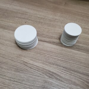 Pode incluir: Tr&ecirc;s pilhas de c&iacute;rculos de papel redondos brancos sobre uma superf&iacute;cie de madeira.
