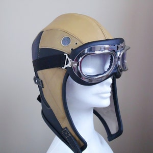 Puede incluir: Un casco de aviador de cuero marr&oacute;n y negro con una visera y gafas cromadas.