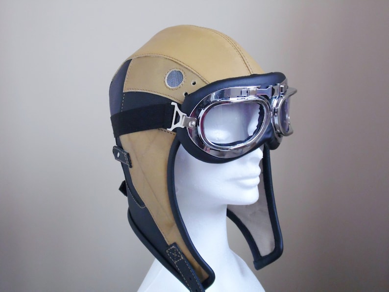 Puede incluir: Un casco de aviador de cuero marr&oacute;n y negro con una visera y gafas cromadas.