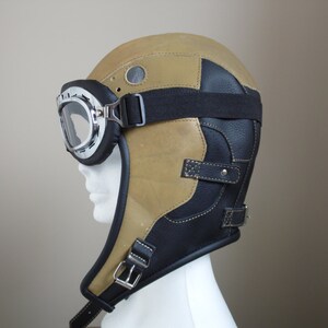 Puede incluir: Un casco de aviador de cuero marr&oacute;n con una correa de barbilla de cuero negro y unas gafas.