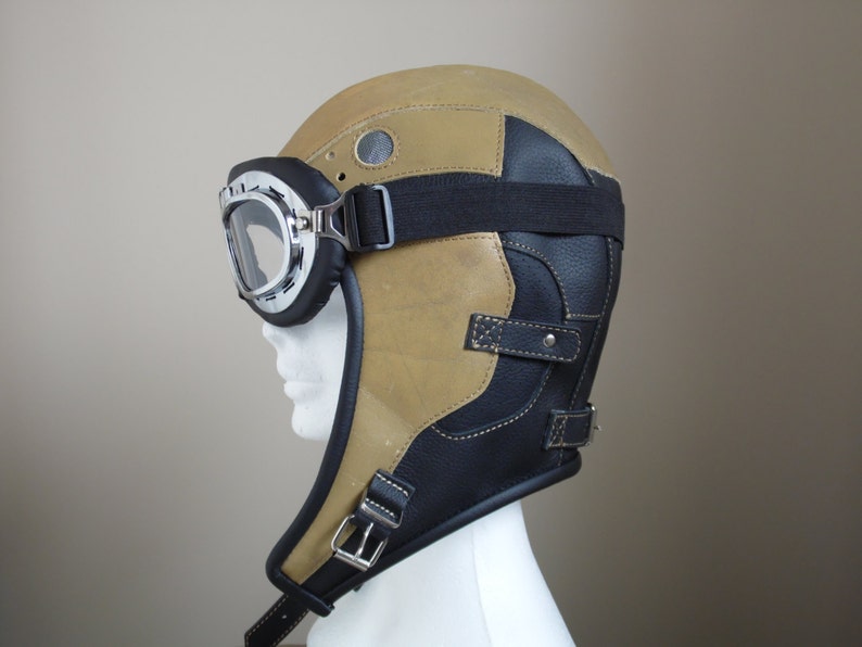 Puede incluir: Un casco de aviador de cuero marr&oacute;n con una correa de barbilla de cuero negro y unas gafas.