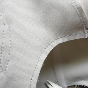 May include: Close-up of a white fabric with stitching along the edges. The fabric is folded over and the stitching is visible on both sides.