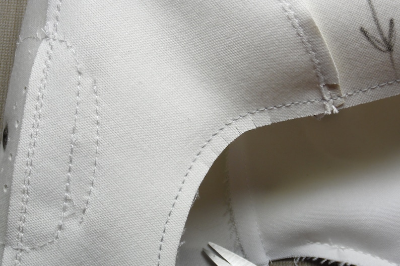 May include: Close-up of a white fabric with stitching along the edges. The fabric is folded over and the stitching is visible on both sides.