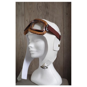 May include: White leather aviator helmet with a brown leather strap and goggles. The helmet has a long flap that can be worn down or up.