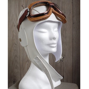 May include: White leather aviator helmet with brown leather straps and a pair of brown leather goggles.