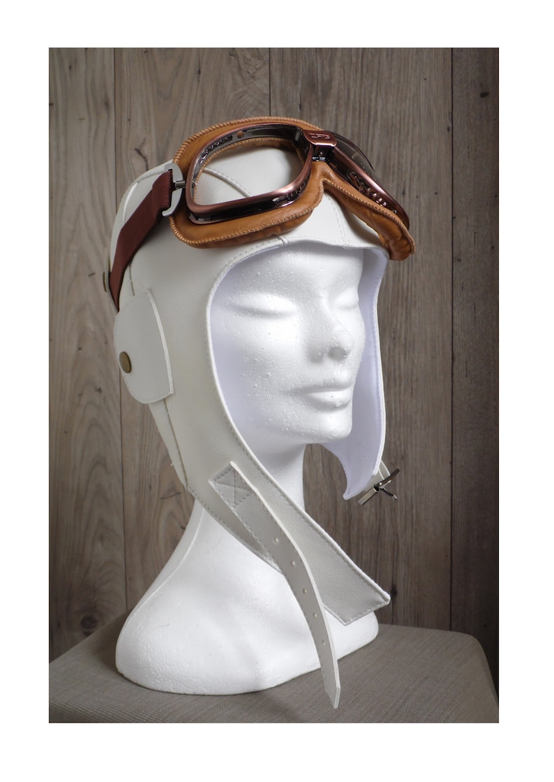 May include: White leather aviator helmet with brown leather straps and a pair of brown leather goggles.