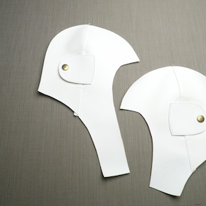 May include: Two white leather helmet patterns with gold button accents.