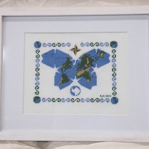May include: A framed cross-stitch embroidery depicting a butterfly with a world map design. The butterfly is blue and green with a yellow and brown world map. The frame is white and the embroidery is surrounded by a blue and green border.