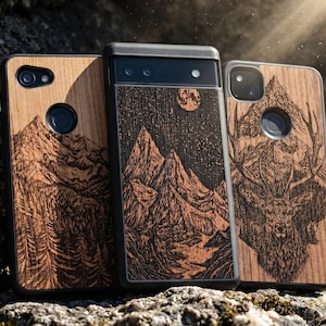 May include: Three wooden phone cases with nature-themed designs. One case features a mountain range, another a starry night scene with mountains and a moon, and the third a deer. The cases are made of wood and have black borders.