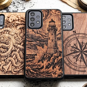 Op de afbeelding: Drie rechthoekige telefoonhoesjes met zwarte randen en achterpanelen met houtnerf. Het linkerhoesje toont een gravure van een octopus en anker, het middelste een vuurtoren op een rotsachtige kust en het rechter een nautisch kompas.