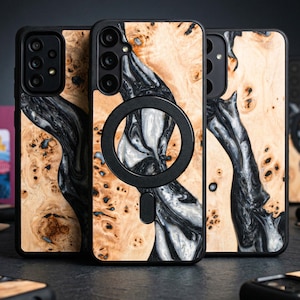 May include: Phone cases with a distinctive wood grain and resin design. The cases display a natural wood pattern with black and white resin accents. One case has a black circular magnetic attachment.