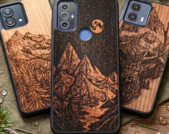 以下が含まれることがあります： 黒い縁取りの木製携帯電話ケース3つ。ケースには、星空の下の山脈、森、鹿の彫刻デザインが施されています。木材は暖かく自然な色合いです。