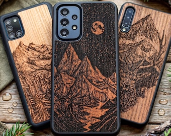 以下が含まれることがあります： 自然をテーマにしたデザインの木製携帯電話ケース3つ。1つのケースは、星空と満月の下の山脈が特徴です。もう1つは山の風景を描き、3つ目は鹿を描いています。すべてのケースには黒い縁があります。
