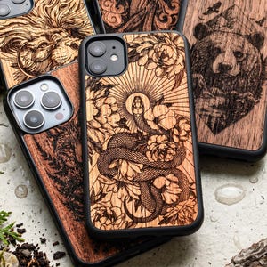 Op de afbeelding: Houten telefoonhoesjes met ingewikkelde lasergesneden ontwerpen. Eén hoesje toont een slang tussen bloemen, een ander een beer en andere leeuwen- en bloempatronen. De hoesjes hebben een zwarte rand en zijn gemaakt van lichtgekleurd hout.