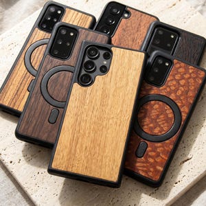 May include: A collection of wooden phone cases in various shades of brown, including light, medium, and dark tones. The cases have a black border and a circular magnetic attachment. The wood grain patterns vary, showcasing natural textures.