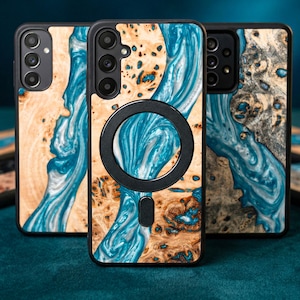 May include: A collection of wooden phone cases with a unique design. The cases feature a combination of light brown wood grain and flowing blue resin, creating a natural, artistic look. Each case has a black border and a circular black magnetic attachment.