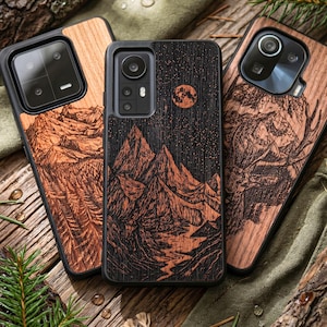 Könnte beinhalten: Drei Handyhüllen aus Holz mit einzigartigen Designs. Eine zeigt eine Bergkette unter einem Sternenhimmel mit Vollmond. Die anderen beiden Hüllen zeigen Berg- und Waldszenen. Die Hüllen haben schwarze Ränder.