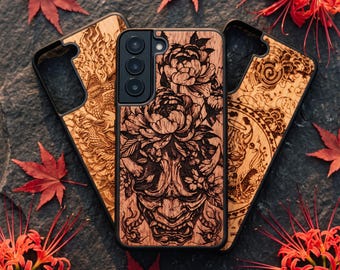 Può includere: Tre cover per telefono con cornici nere e pannelli posteriori in legno chiaro con dettagliati disegni incisi al laser. La cover centrale mostra una maschera Hannya circondata da peonie, mentre quelle laterali presentano motivi a drago.