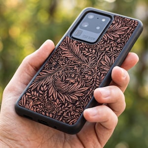 May include: A black phone case with a detailed floral pattern in shades of brown and tan. The case has a black border and a camera lens cutout. The phone case is designed for a Samsung Galaxy S20 Ultra, with "100X" printed on the camera.