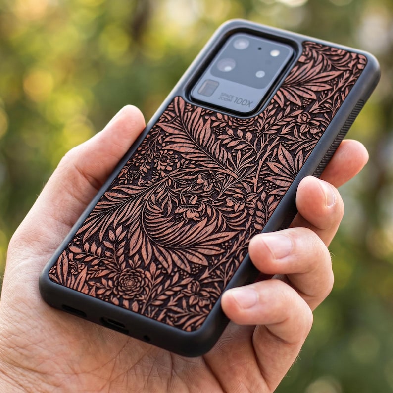 May include: A black phone case with a detailed floral pattern in shades of brown and tan. The case has a black border and a camera lens cutout. The phone case is designed for a Samsung Galaxy S20 Ultra, with "100X" printed on the camera.