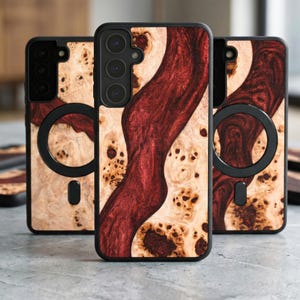 Può includere: Tre custodie per telefono con un design a venature del legno. Le custodie hanno un bordo nero e un motivo in legno naturale con un intarsio in resina rosso scuro. Le custodie hanno un attacco magnetico circolare sul retro.