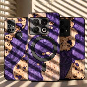 Può includere: Tre custodie per telefono con un design unico. Le custodie presentano un motivo a venature di legno viola e beige. La custodia centrale ha una caratteristica circolare nera. Le custodie hanno ritagli per la fotocamera.