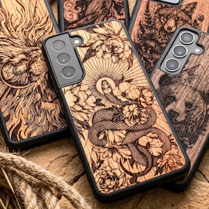 May include: A selection of wooden phone cases with detailed laser-cut designs. One case shows a snake and flowers, others feature a lion, a bear, and a forest. The cases have a natural wood grain finish and black edges. The cases are made of wood.
