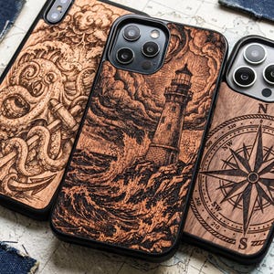 May include: Three smartphone cases with wood-grain back panels featuring laser-engraved designs. The left case shows an octopus and anchor, the centre case depicts a lighthouse with stormy waves, and the right case displays a nautical compass.