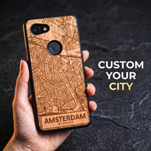 May include: A wooden phone case featuring a detailed map of Amsterdam, Netherlands. The case has a black border and the city name is displayed at the bottom. The text "CUSTOM YOUR CITY" is visible in the background.