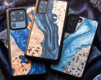May include: Three smartphone cases featuring a combination of natural light-colored wood burl and swirling blue resin. Each case has a black frame and a camera cutout, showcasing a unique marbled pattern where the wood grain meets the blue resin.