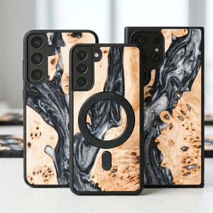 Puede incluir: Tres fundas para teléfono con diseño de vetas de madera y resina negra. Las fundas tienen un borde negro y un accesorio magnético circular. La veta de la madera es marrón claro con remolinos grises oscuros y negros.