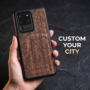 Peut inclure: Coque de smartphone noire avec une carte en bois de Londres, Royaume-Uni. La coque est tenue dans une main. Le texte "CUSTOM YOUR CITY" est affiché en blanc et or. Le design est gravé sur le bois.