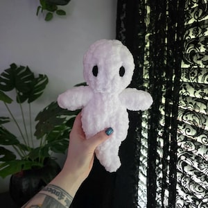 May include: A handmade white plush ghost doll with black button eyes and outstretched arms. The ghost is made of a soft, fuzzy material. The doll is a cute, whimsical design.