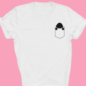 Puede incluir: Camiseta blanca con una silueta negra de una persona asomándose desde un bolsillo. El texto "FELLOW FRIENDS" está impreso debajo del bolsillo.