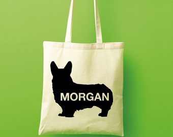 May include: A beige tote bag with a black silhouette of a corgi dog and the name "MORGAN" printed on the front.