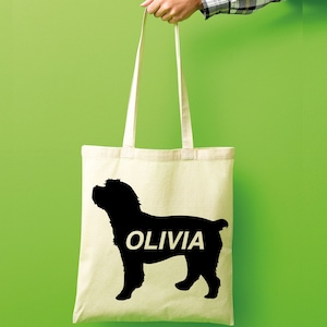 Op de afbeelding: Een witte canvas tote bag met een zwart silhouet van een hond en de naam "Olivia" in wit gedrukt.