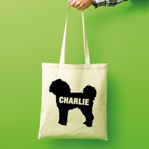 Op de afbeelding: Een witte canvas tote bag met een zwart silhouet van een hond en de naam "CHARLIE" erop gedrukt.