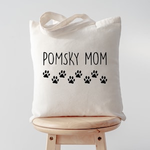 May include: White canvas tote bag with black text that reads "Pomsky Mom" and a row of black paw prints.