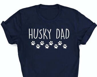 May include: A navy blue t-shirt with the text "Husky Dad" in white lettering and a row of white paw prints below the text.