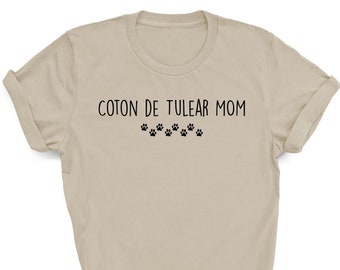 May include: A beige t-shirt with the text "Coton de Tulear Mom" and a row of paw prints.