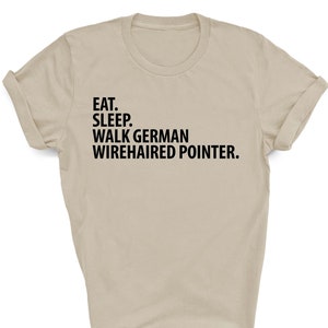 May include: A beige t-shirt with black text that reads "Eat. Sleep. Walk German Wirehaired Pointer."