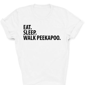 Può includere: T-shirt bianco con la scritta "EAT. SLEEP. WALK PEEKAPOO." in nero, centrata sul davanti. La maglietta ha maniche corte e girocollo. Il tessuto sembra essere cotone o un materiale simile.