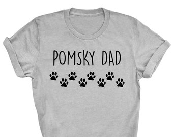 May include: A light gray t-shirt with the text "POMSKY DAD" in black, above a row of seven black paw prints. The shirt has rolled-up sleeves and a crew neck.