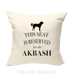 May include: A white throw pillow with black text that reads "This seat is reserved for the Akbash" and a black silhouette of an Akbash dog.