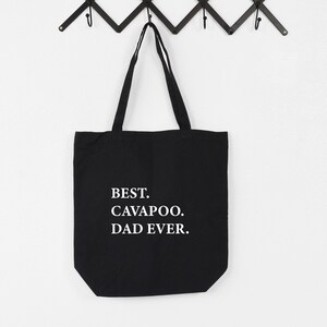 Op de afbeelding: Zwarte canvas tote bag met witte tekst die "BEST. CAVAPOO. DAD EVER." zegt.